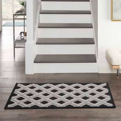 Black-and-white diamond lattice rug with a black border, placed in front of stairs in a modern entryway.