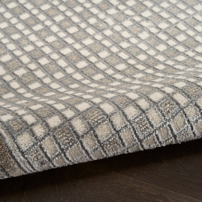 Soft area rug with gray & ivory checker grid pattern, plush textured pile, folded edge on dark wood floor.