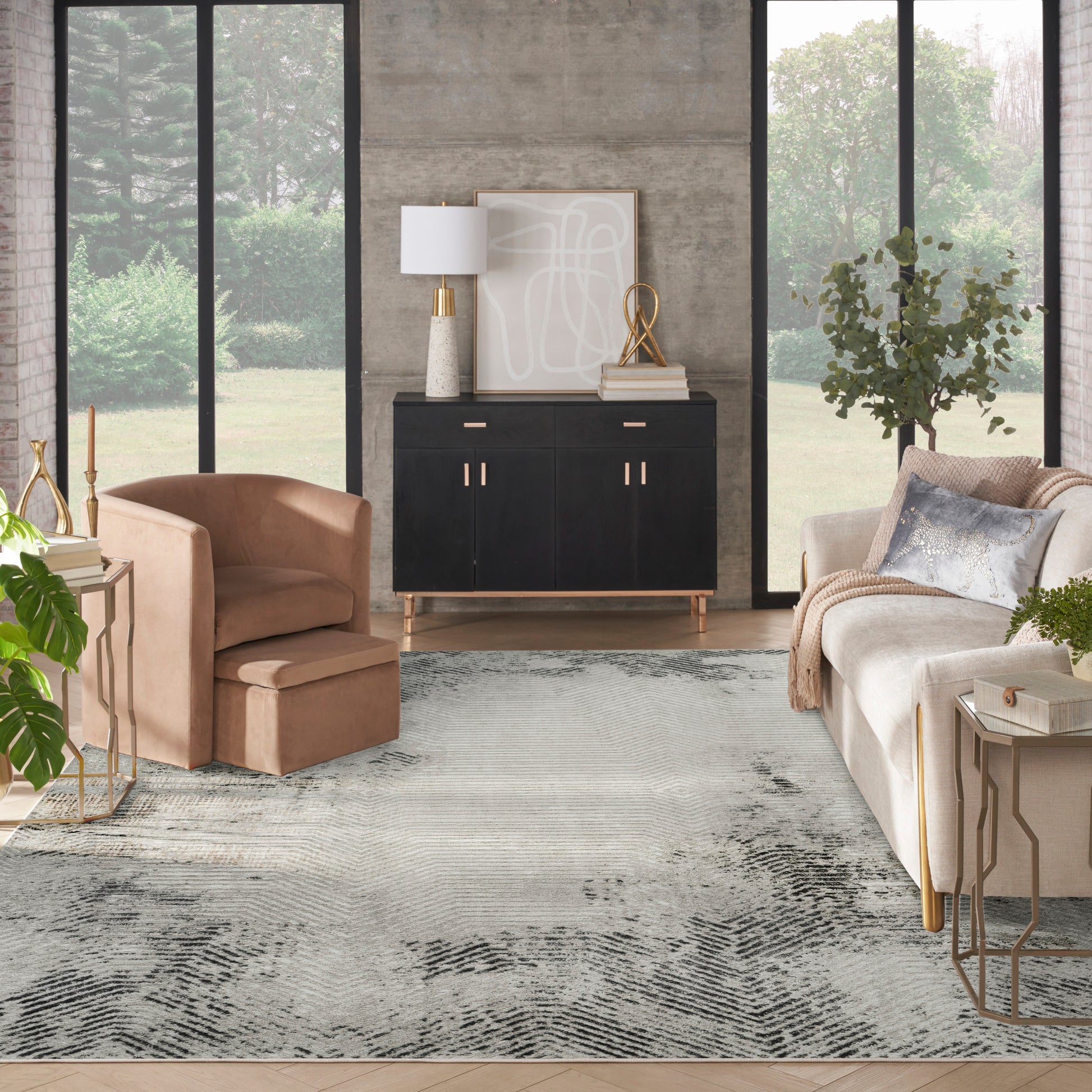 Modern living room with black sideboard, beige sofa, blush armchair, abstract art, gold accents, concrete wall, and gray rug.
