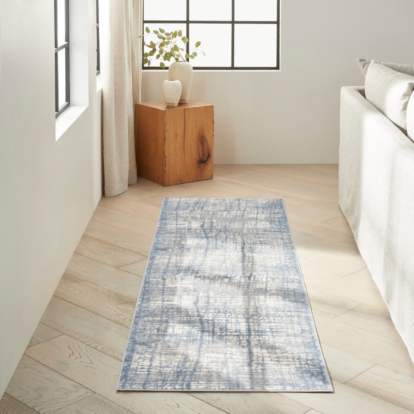 Blue-gray distressed rectangular runner rug on light wood floor beside beige sofa, wooden cube side table with vases.