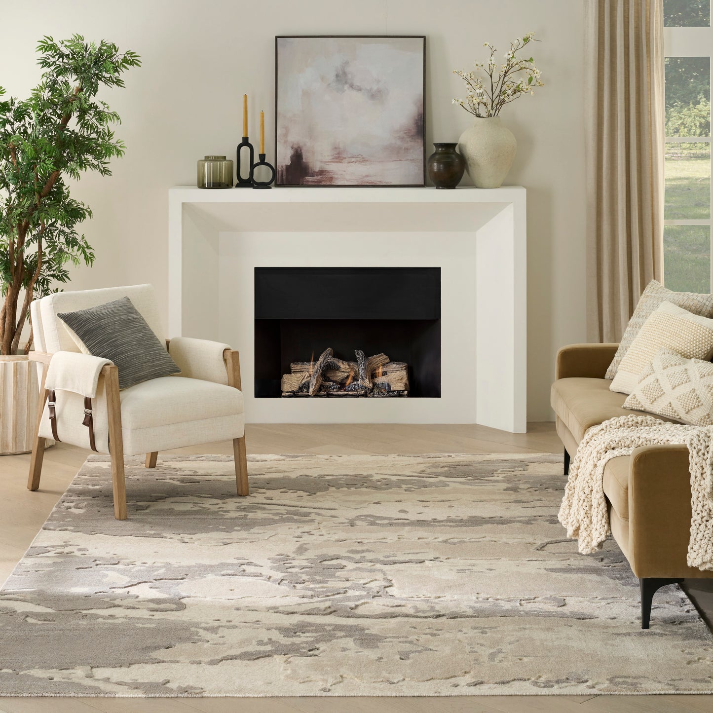Neutral living room with white fireplace, beige sofa and armchair, abstract gray-beige rug, wood accents and greenery.