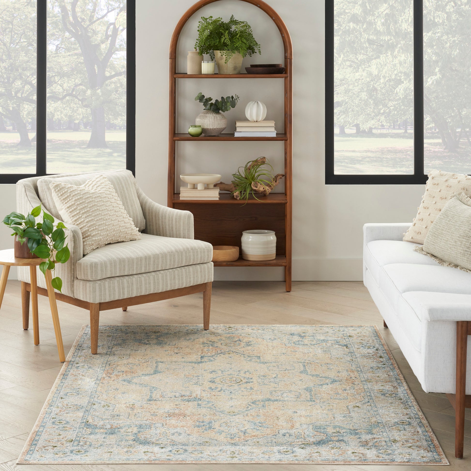 Cozy living room with arched wooden bookcase, beige striped armchair, white sofa, blue-toned rug, and green potted plants.