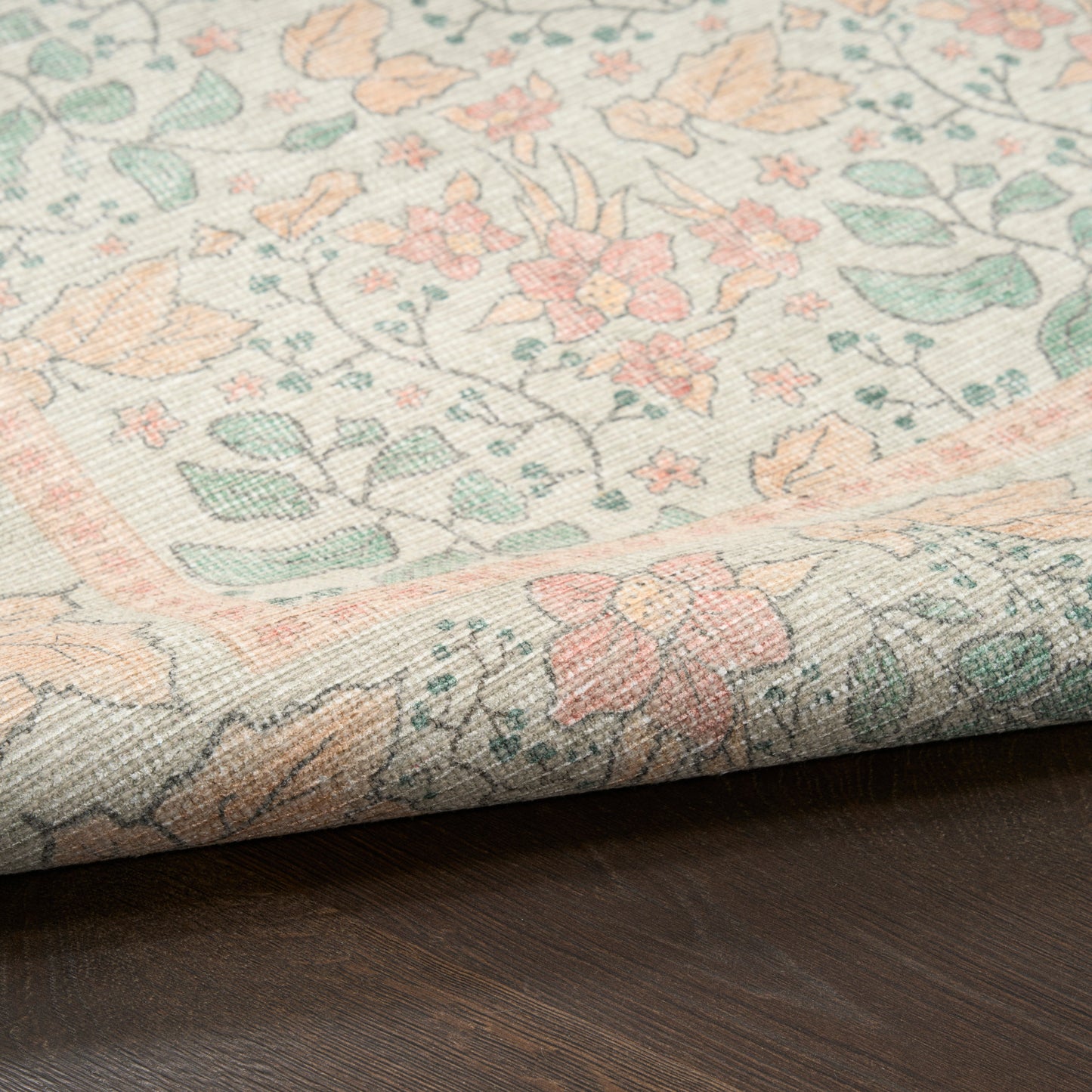 Pastel floral vintage-style runner rug in peach, mint, pink and ivory; woven texture on dark wood floor.