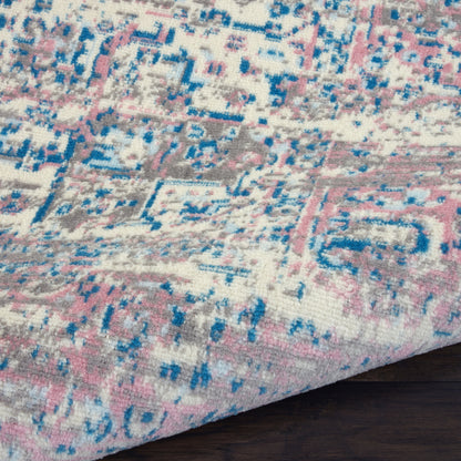 Pastel pink & blue geometric woven rug with cream background, close-up edge on dark hardwood.