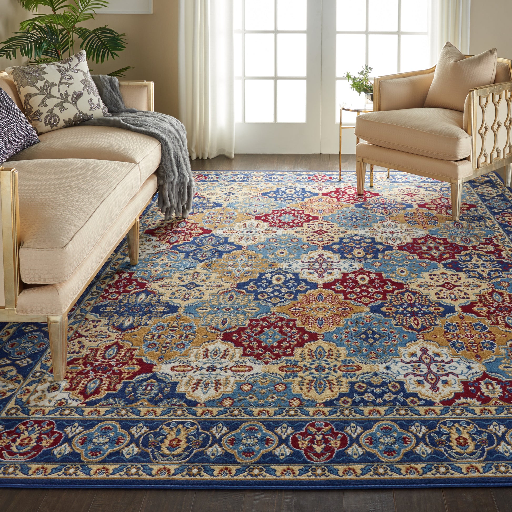 Cozy living room with an ornate blue, red, gold oriental area rug on the floor, with cream fabric sofas and light wood chairs.