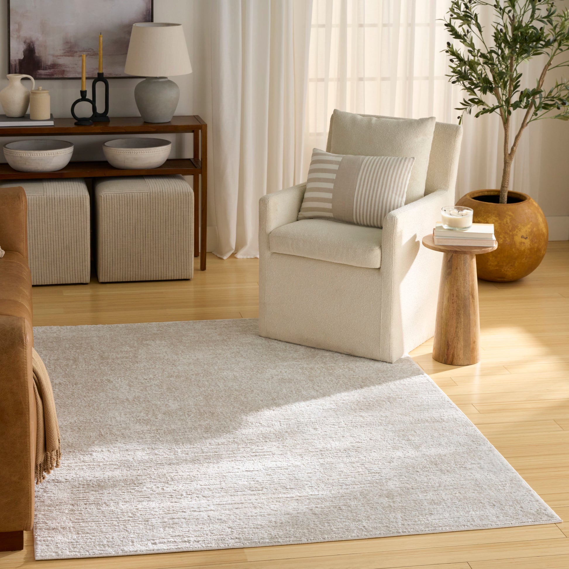 Light gray rug in a living area with a cream upholstered armchair with a striped beige cushion, a round wood side table, and a potted plant.
