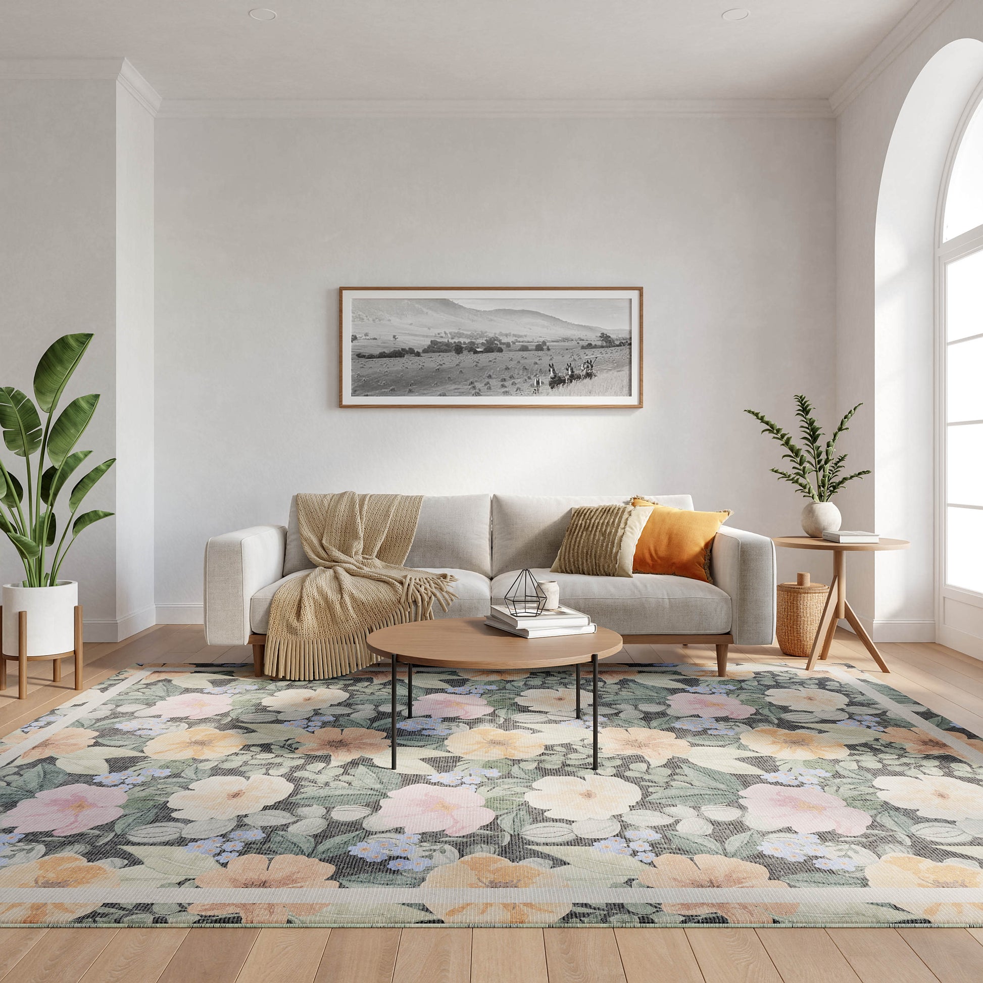 Light gray sofa with beige throw and orange pillow, round wooden coffee table on a pastel floral rug with potted plants.