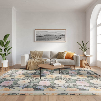 Light gray sofa with beige throw and orange pillow, round wooden coffee table on a pastel floral rug with potted plants.