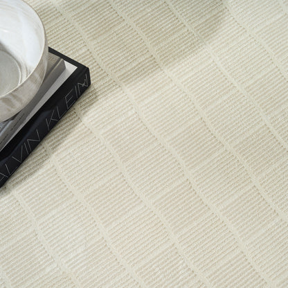Cream textured rug with square grid pattern; white ceramic cup on a dark rectangular book.