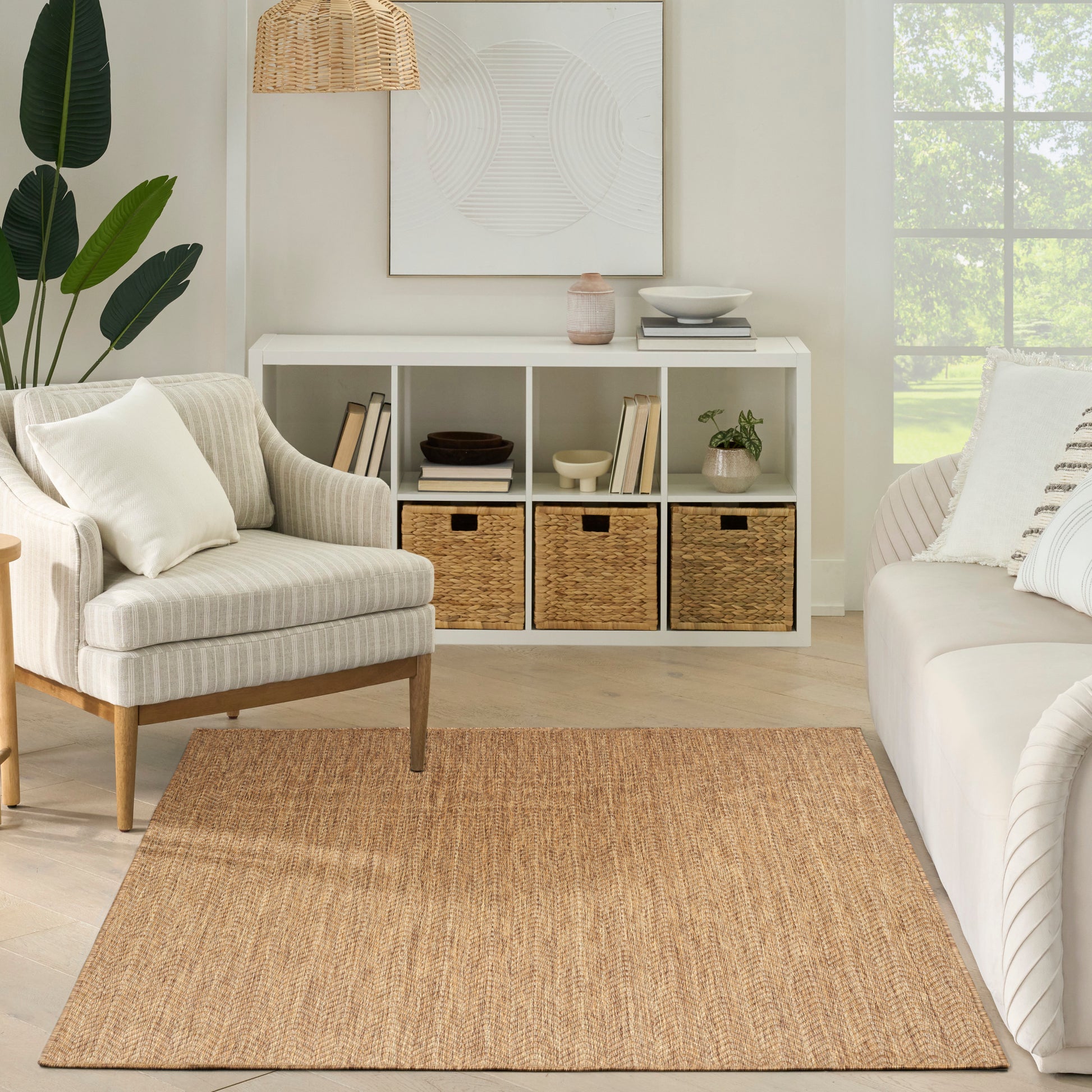 Neutral living room with a jute rug, white cube storage, woven baskets, striped armchair, wicker pendant lamp, and a large window.