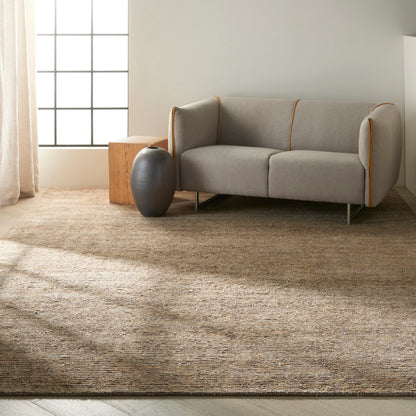 Light gray sofa with orange piping on a textured tan rug, beside a dark ceramic vase and a wooden cube side table.