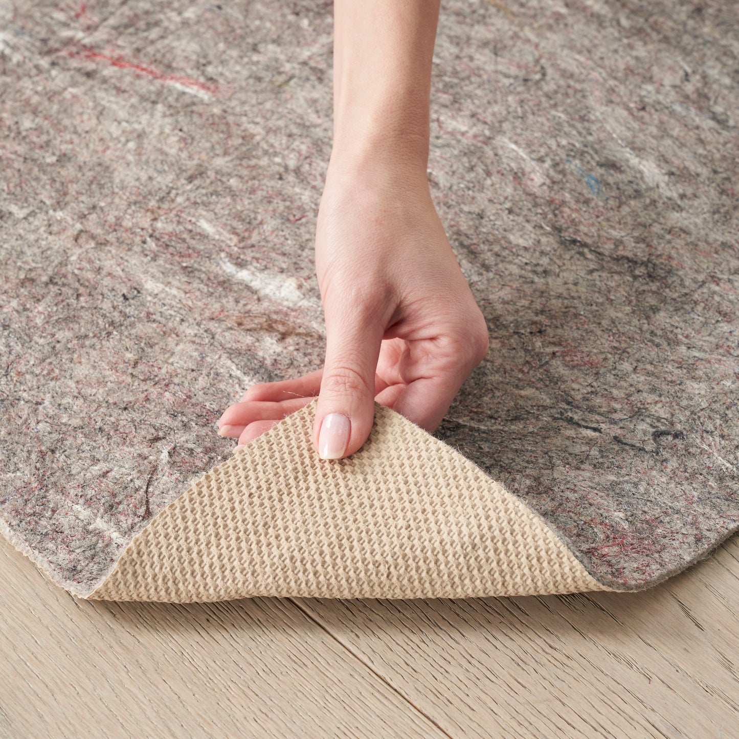 Hand lifting a grey speckled neutral runner rug to reveal its beige waffle-textured underside on a wood floor.