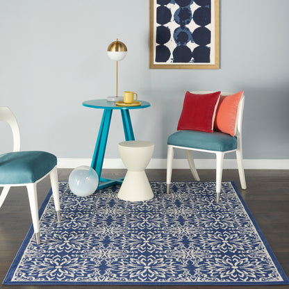 Blue round table with teal legs, white chair with teal seat, coral and red cushions, navy patterned rug, navy wall art.
