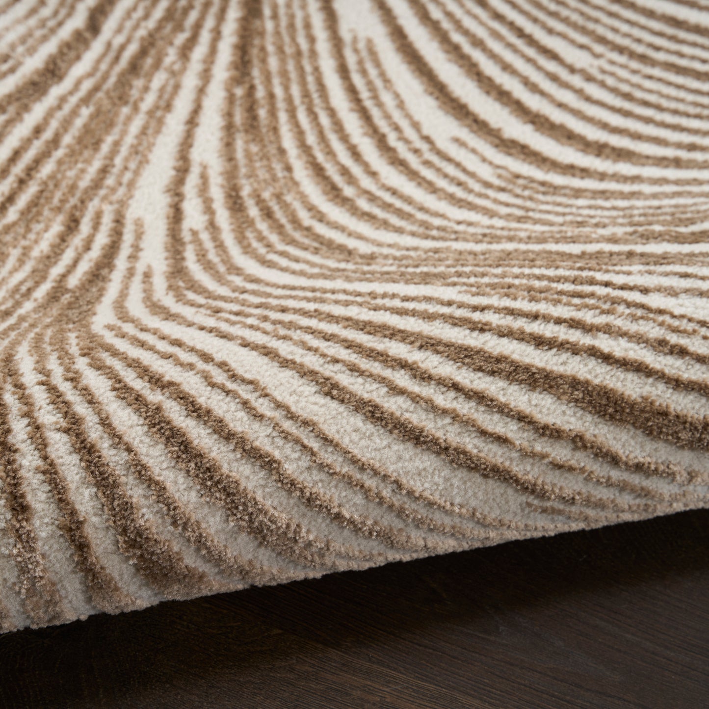 Close-up of a beige-brown zebra-striped shag rug with a textured pile on dark hardwood floor.
