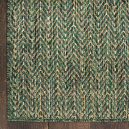 Green and cream chevron woven rug with herringbone zigzag pattern, rectangular, on dark wood floor.