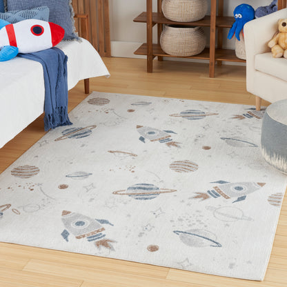 Rectangular, soft light-cream space-themed area rug with blue rockets and planets on a wooden floor in a kids' bedroom.