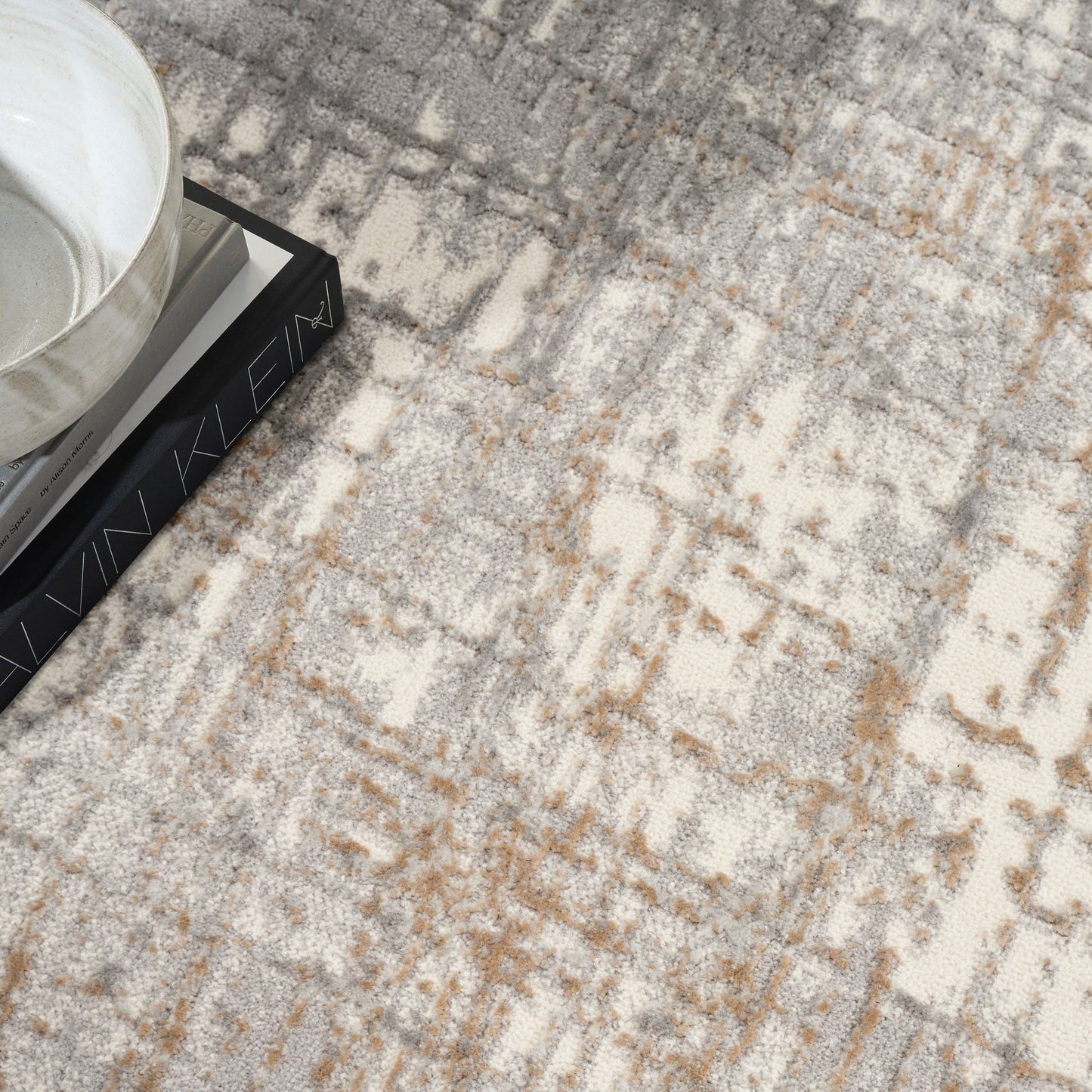 Beige and gray abstract-pattern area rug with a ceramic bowl on a stack of books.
