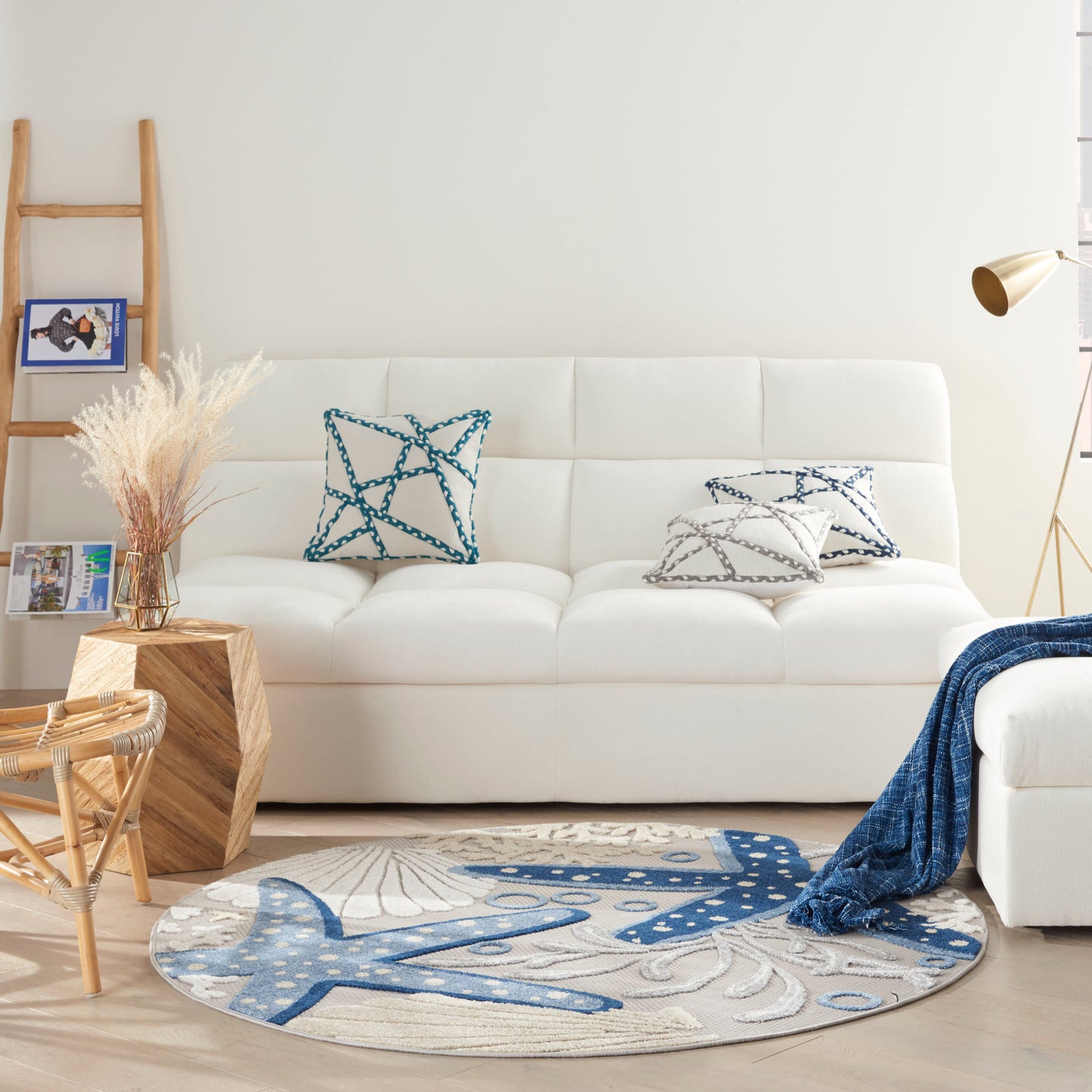 Round blue-and-white nautical rug with abstract sea pattern under a white sofa in a bright living room.