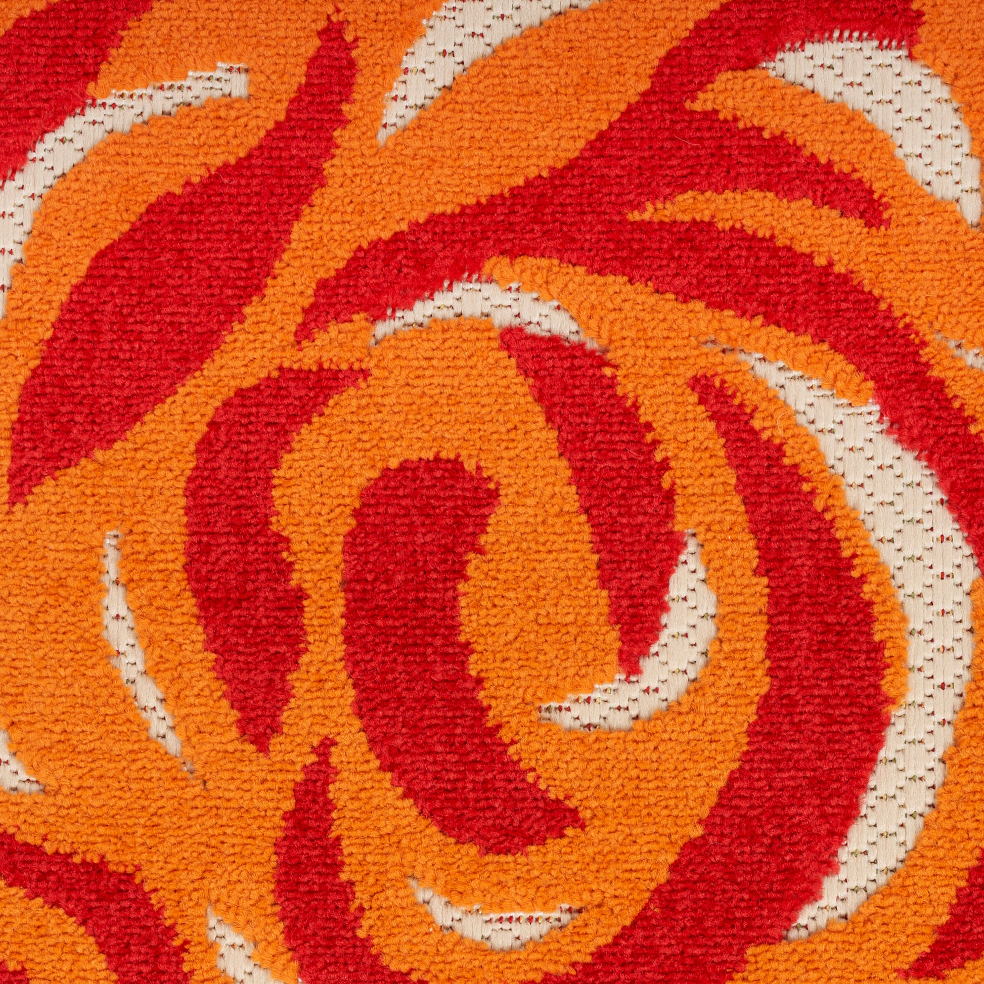 Close-up of a tufted rug with orange and red swirling flame-like patterns and cream accents.