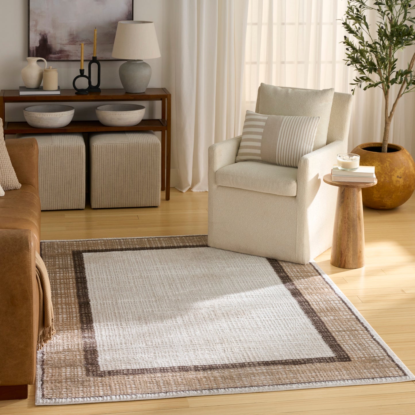 Cream upholstered armchair with striped cushion, wooden side table, and a beige-brown bordered rug on a light wood floor.