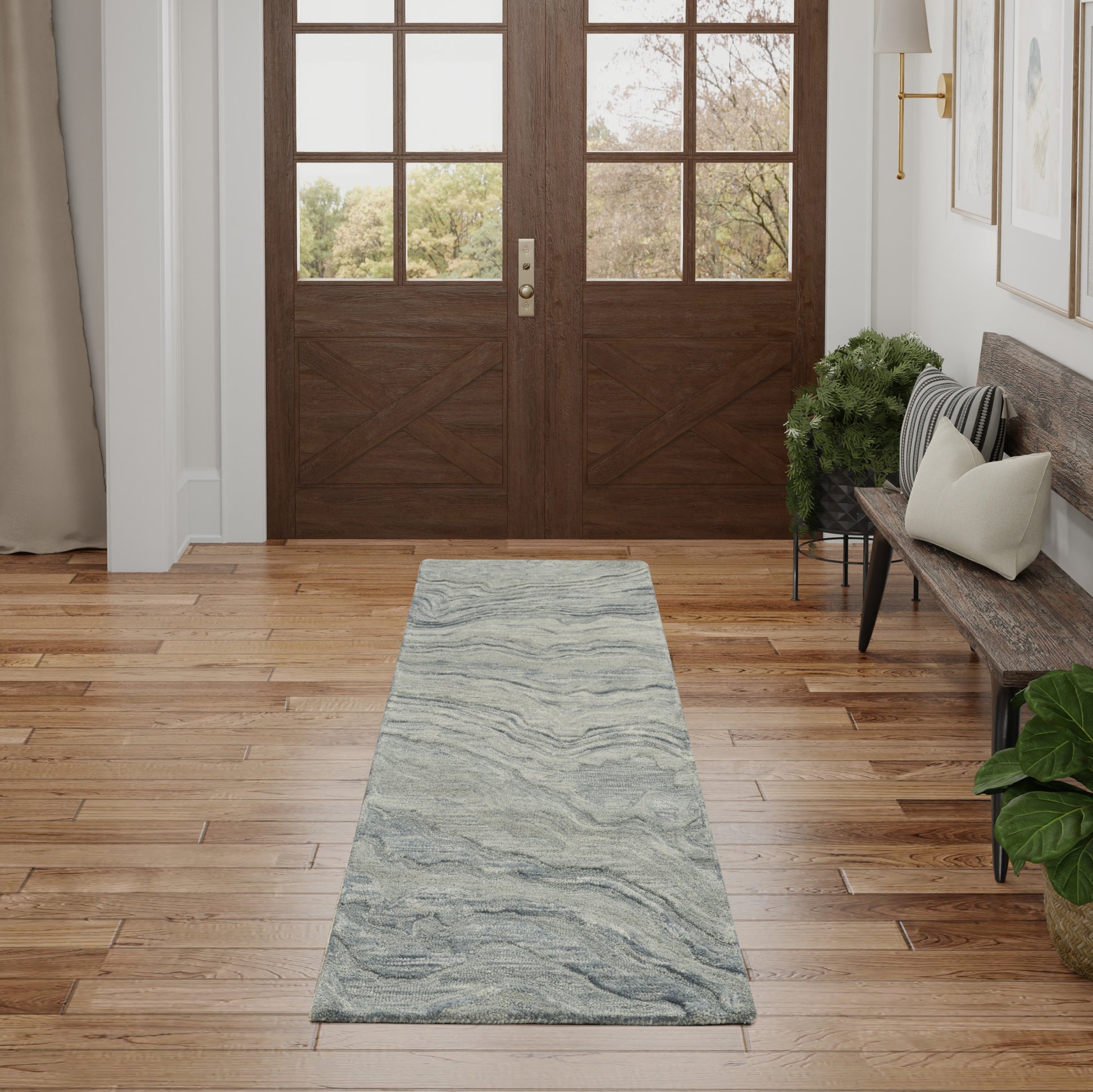Gray-blue marbled runner rug on warm hardwood entry floor with double wooden doors, bench, and plants.