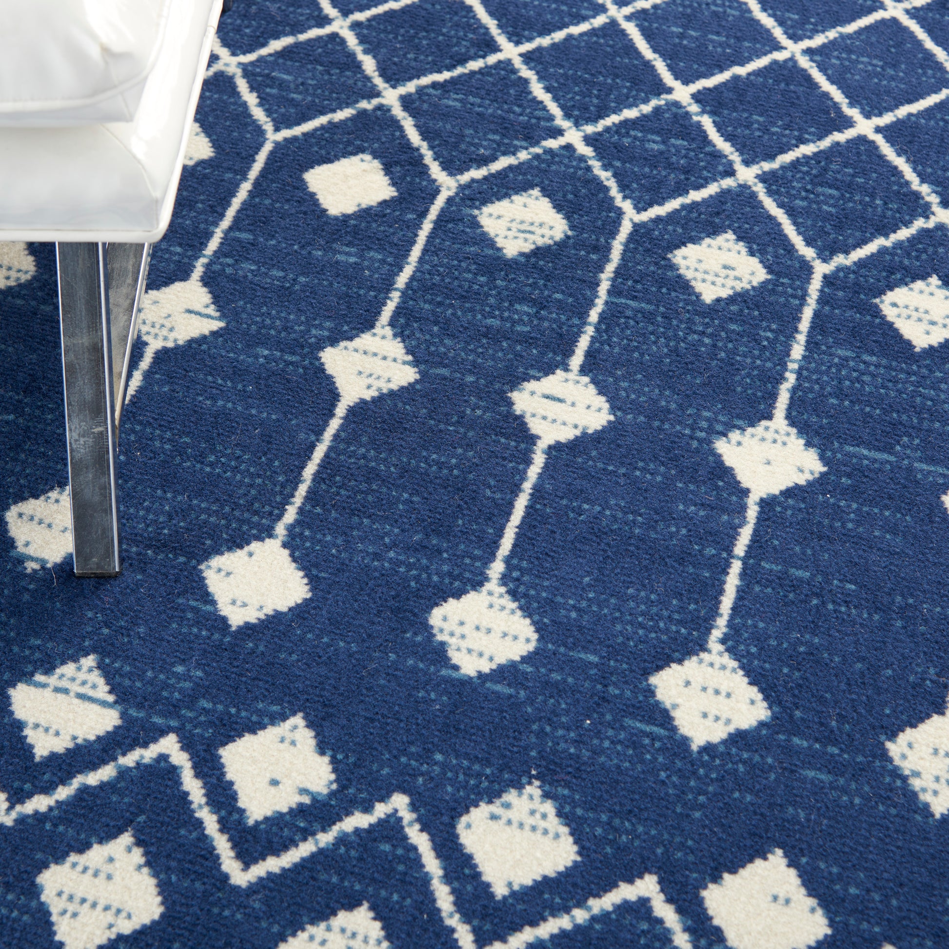 Blue area rug (6' x 9') with white geometric lattice and diamond motifs; partial white chair leg visible.