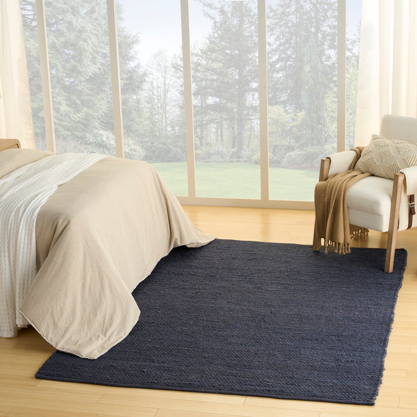 Rectangular dark navy rug on light wood floor in a bright bedroom with beige bedding and a white chair by large windows