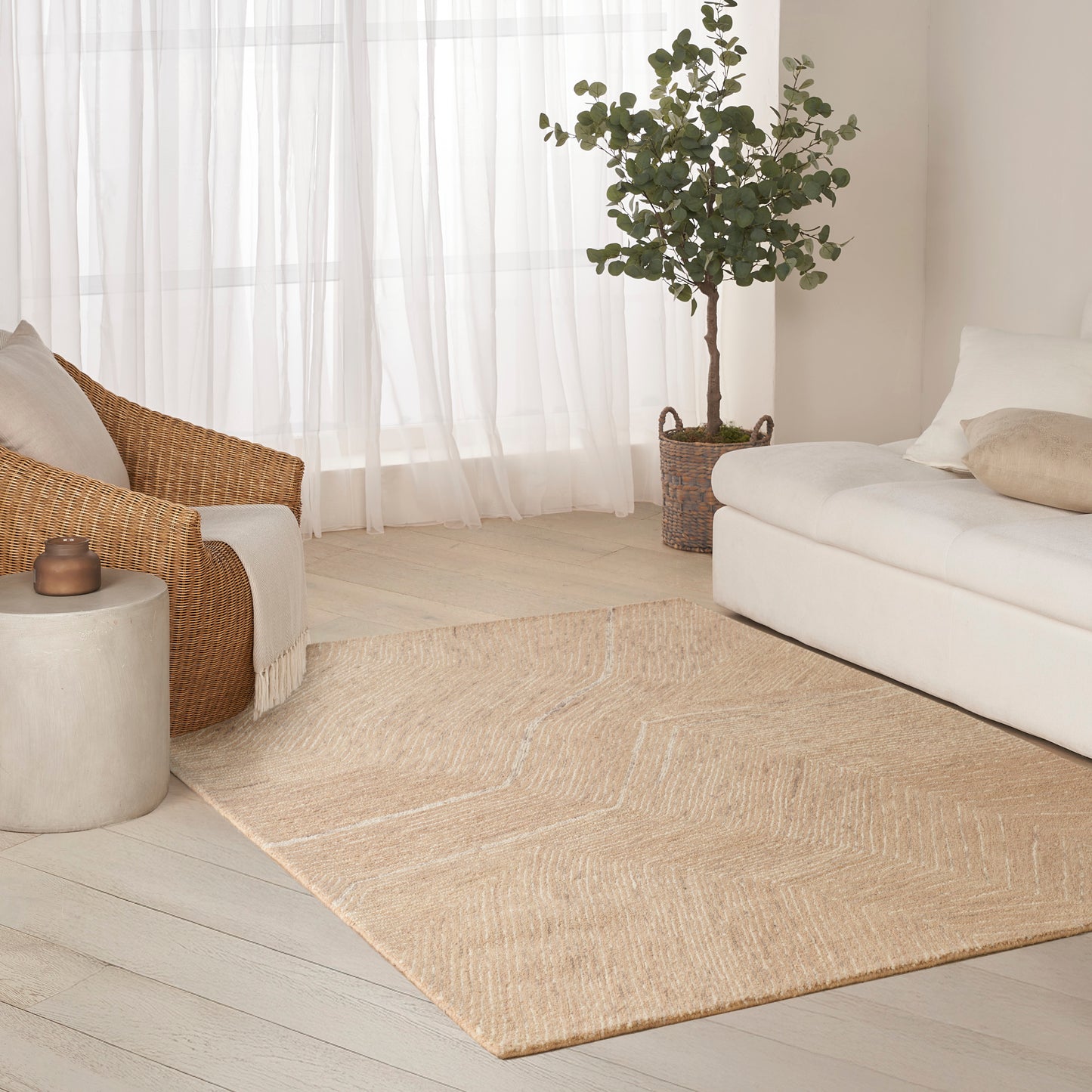 Natural jute area rug on light wood floor in airy living room with white sofa, wicker chair, and potted plant.
