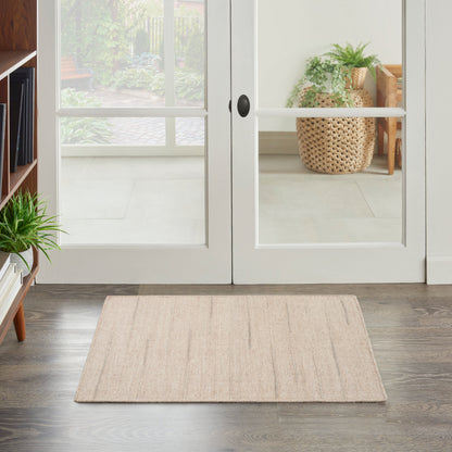 Beige rectangular area rug with subtle texture on dark wood floor in bright entryway.