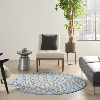 Round blue geometric rug in a living room with cream chair, black pillow, gray side table, leather couch, and tall plant.