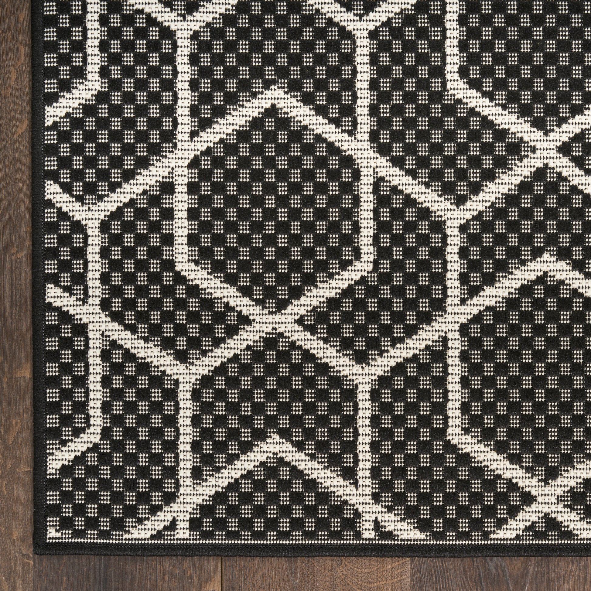 Black and ivory geometric rug with interlocking hexagons, textured flat-weave, on dark wood floor.