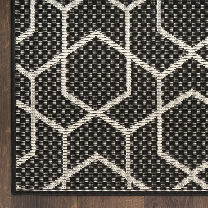 Black and ivory geometric rug with interlocking hexagons, textured flat-weave, on dark wood floor.