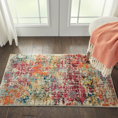 Rectangular abstract multicolor area rug on dark hardwood floor, beside a chair with an orange fringed throw.
