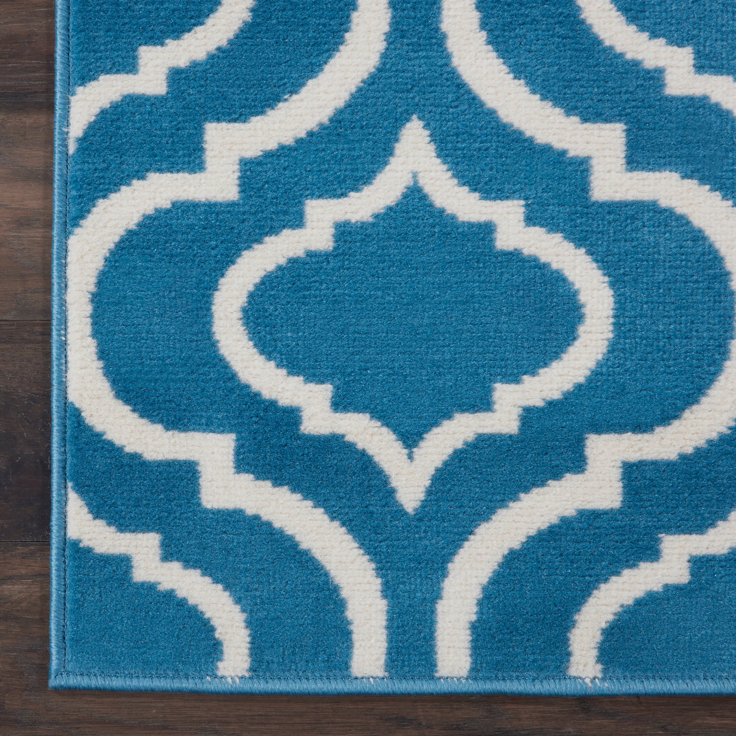 Blue rug with white Moroccan trellis pattern, plush pile and bound edge on dark wood floor.