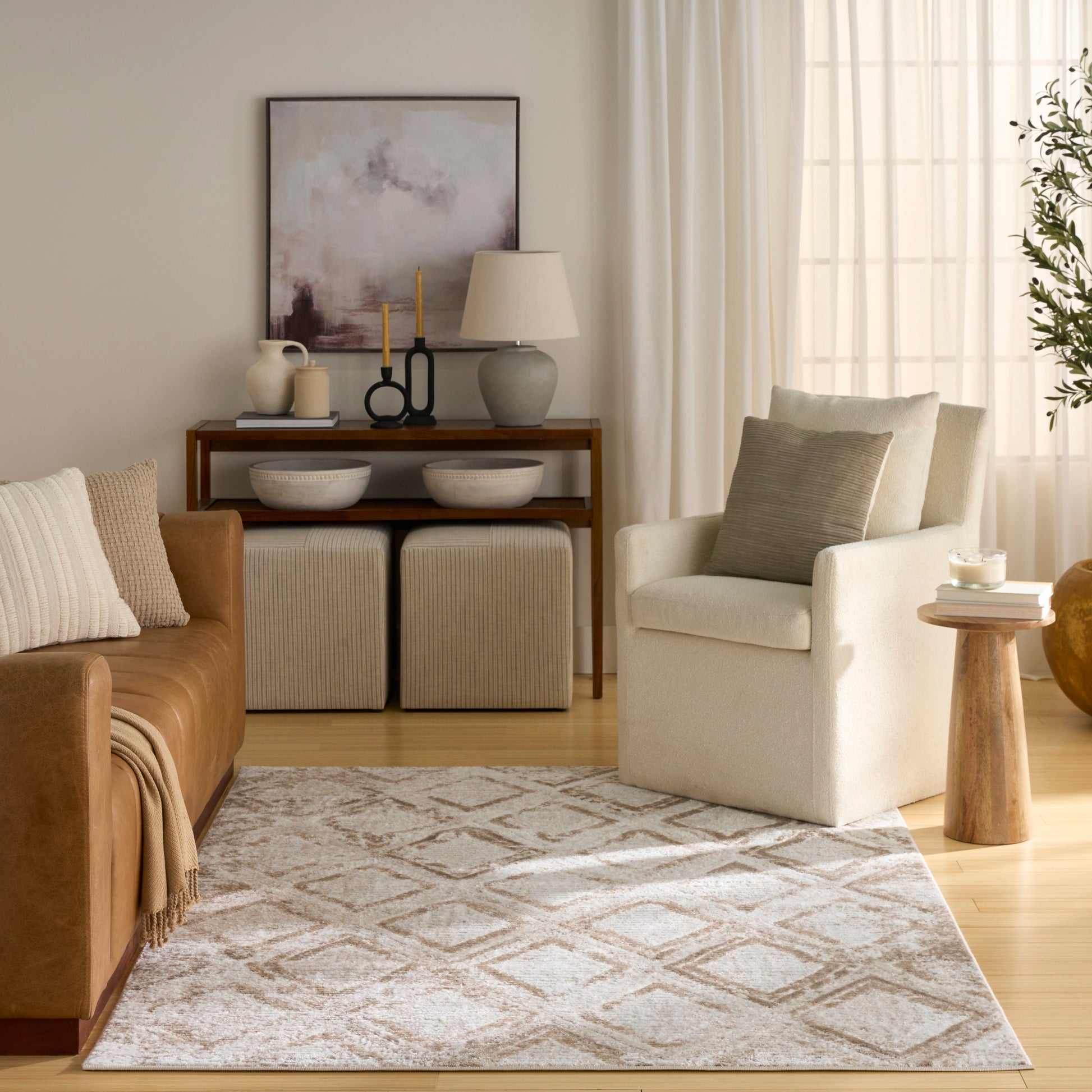 Neutral living room with brown leather sofa, cream armchair, beige rug, wooden console, & window with sheer curtains.