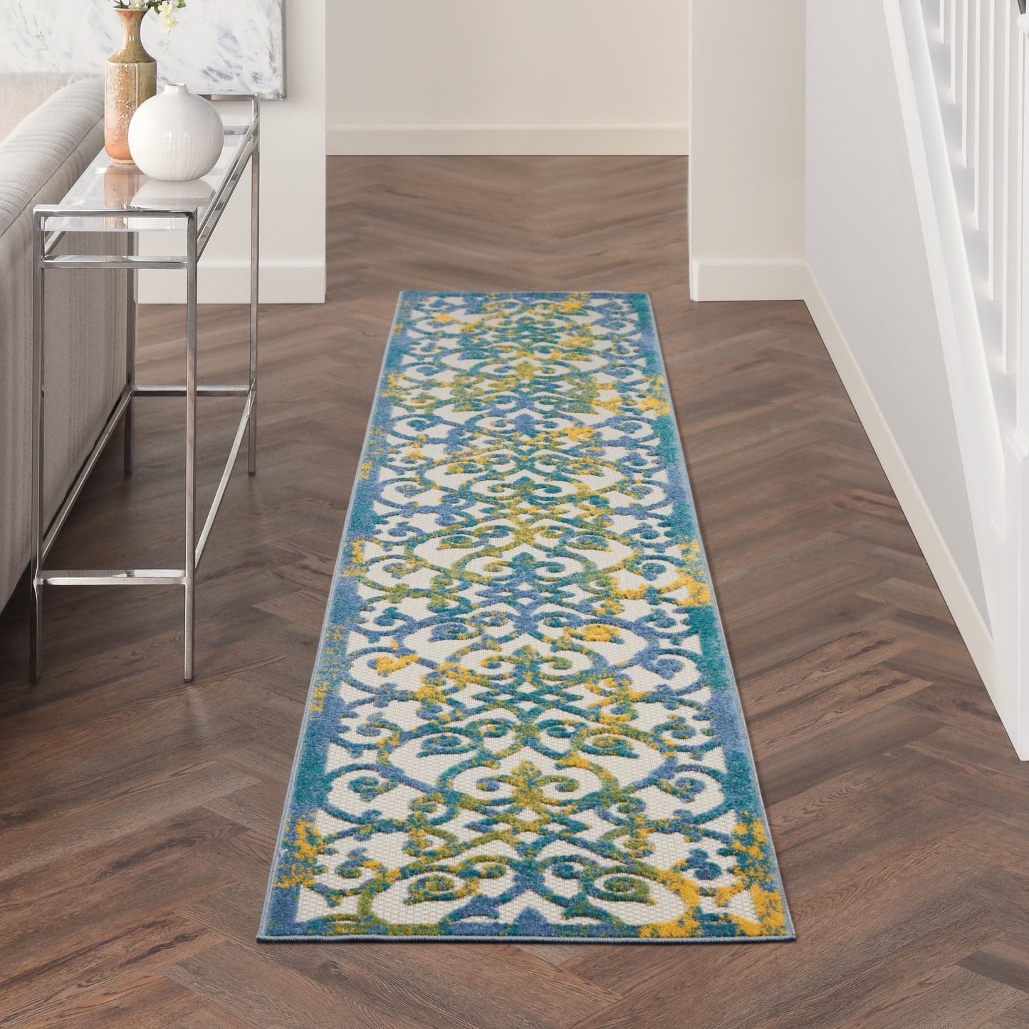 Narrow hallway runner rug with blue border & teal-gold arabesque scroll pattern on white, laid on dark wood floor.