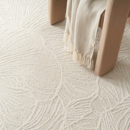 Cream textured rug with an abstract leaf pattern, beige furniture legs, and fringe-draped fabric.