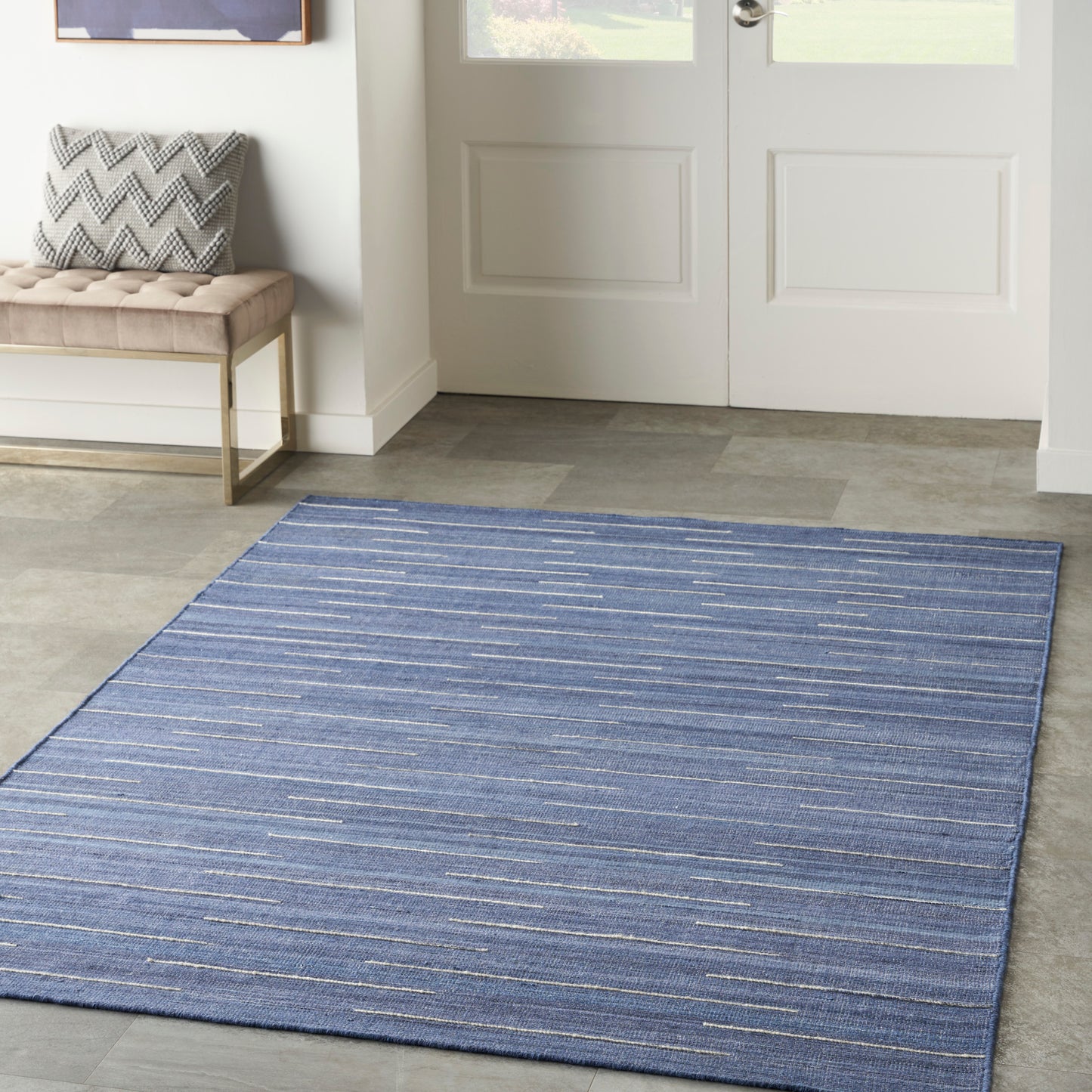 Blue striped area rug in entryway on gray tile, with bench and chevron pillow beside door.