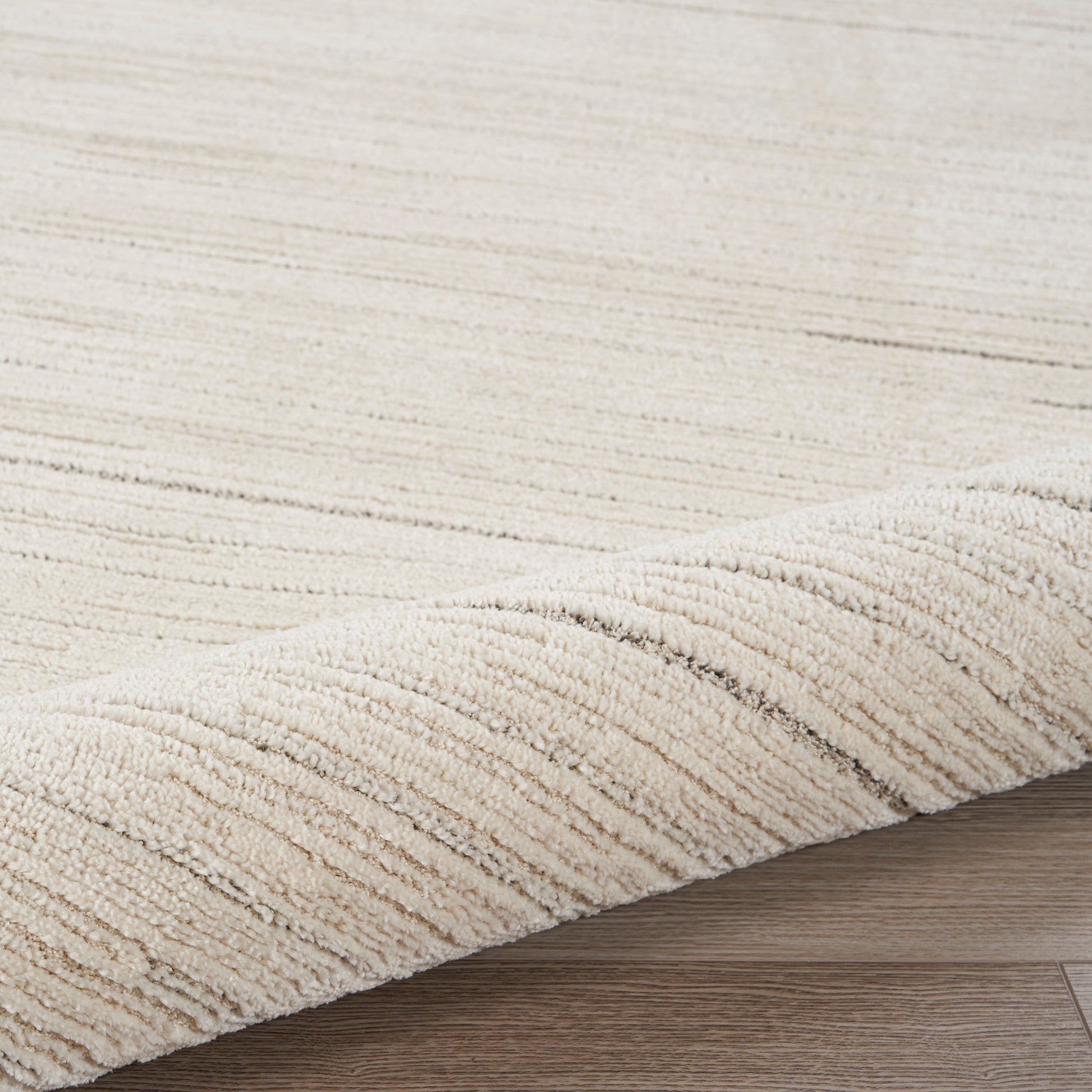 Cream textured runner rug with subtle stripes, partially rolled on a light wooden floor; plush, neutral living-room rug.