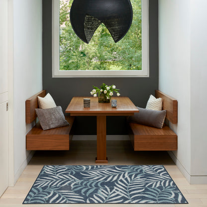 Walnut built-in banquette with cushions around a rectangular table, dark wall, large window, black pendant light, & blue leaf rug.