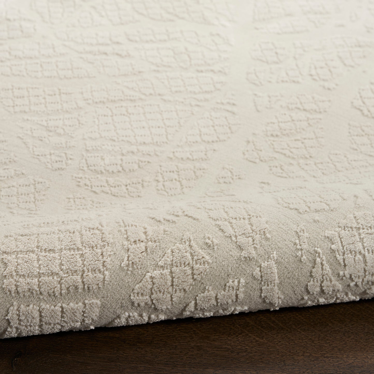Cream textured area rug with embossed geometric pattern and soft pile, rolled edge on dark wood floor