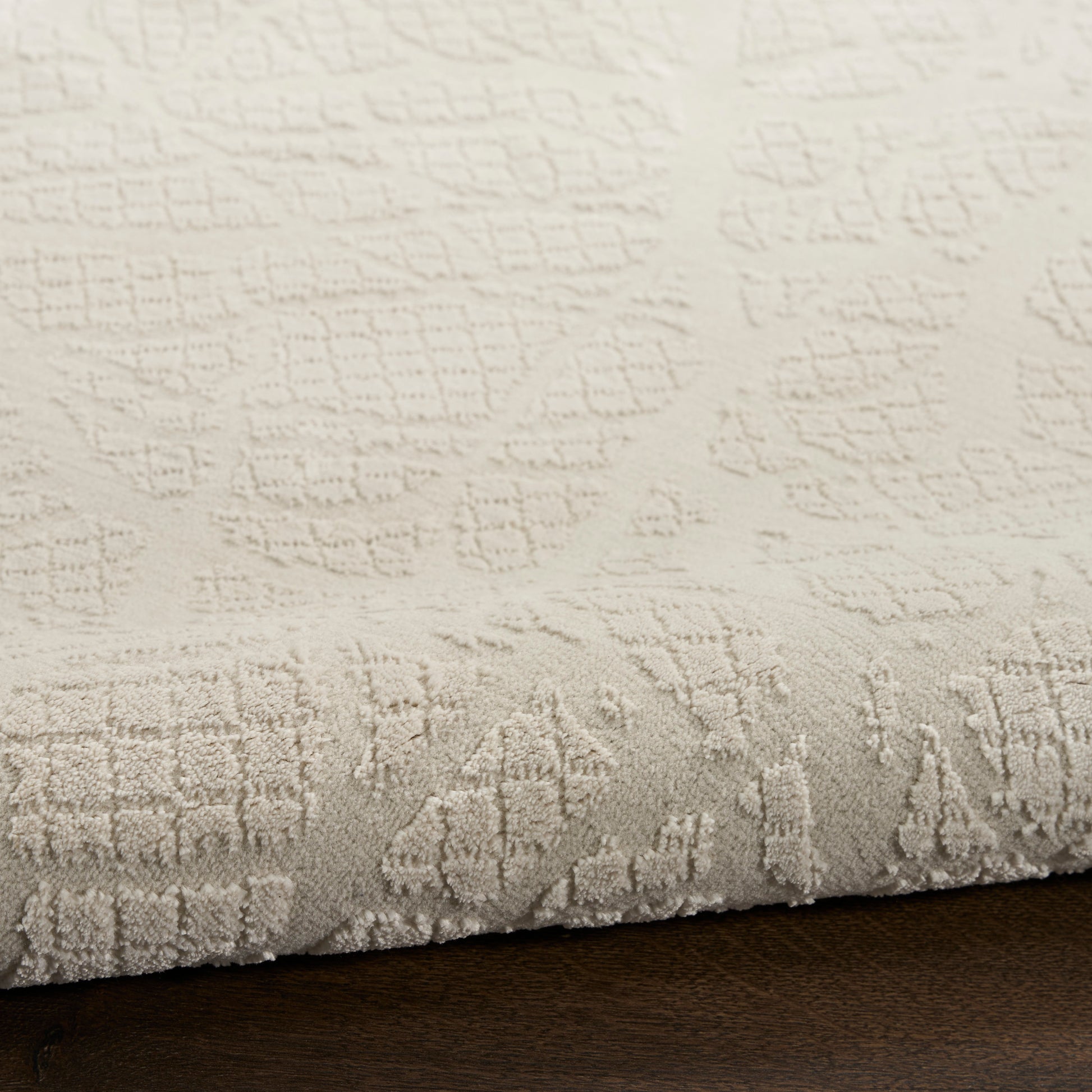 Cream textured area rug with embossed geometric pattern and soft pile, rolled edge on dark wood floor