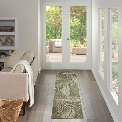 Bright outdoor seating area with a beige outdoor sofa, cream throw, and a long green leaf-pattern 6' runner rug, with glass doors to a wicker patio.