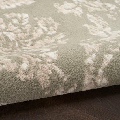 Close-up of a plush rug with cream floral damask pattern on sage green background, edge resting on dark wood floor.