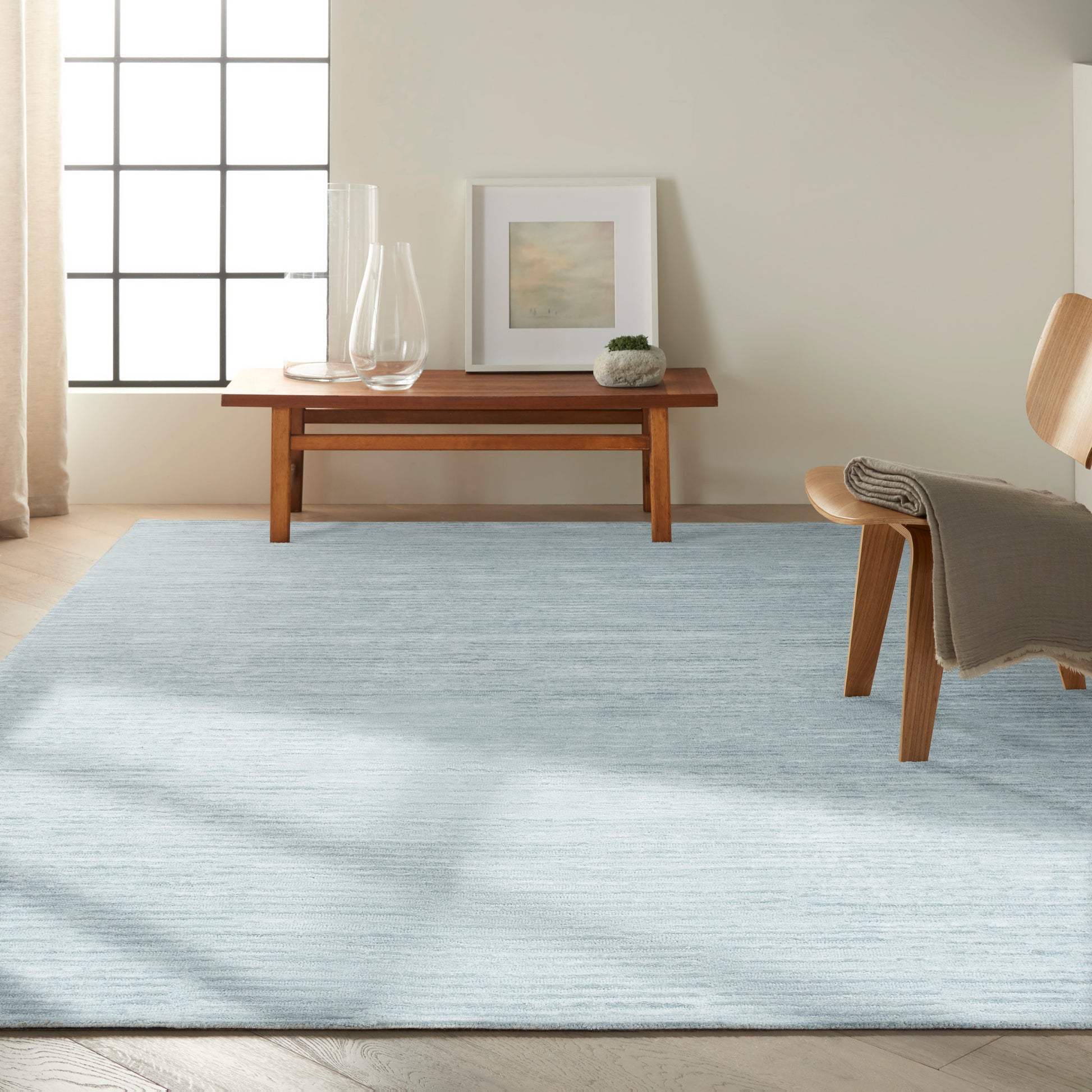 Light blue, textured rectangular area rug in a modern living room with a wooden coffee table and chair.