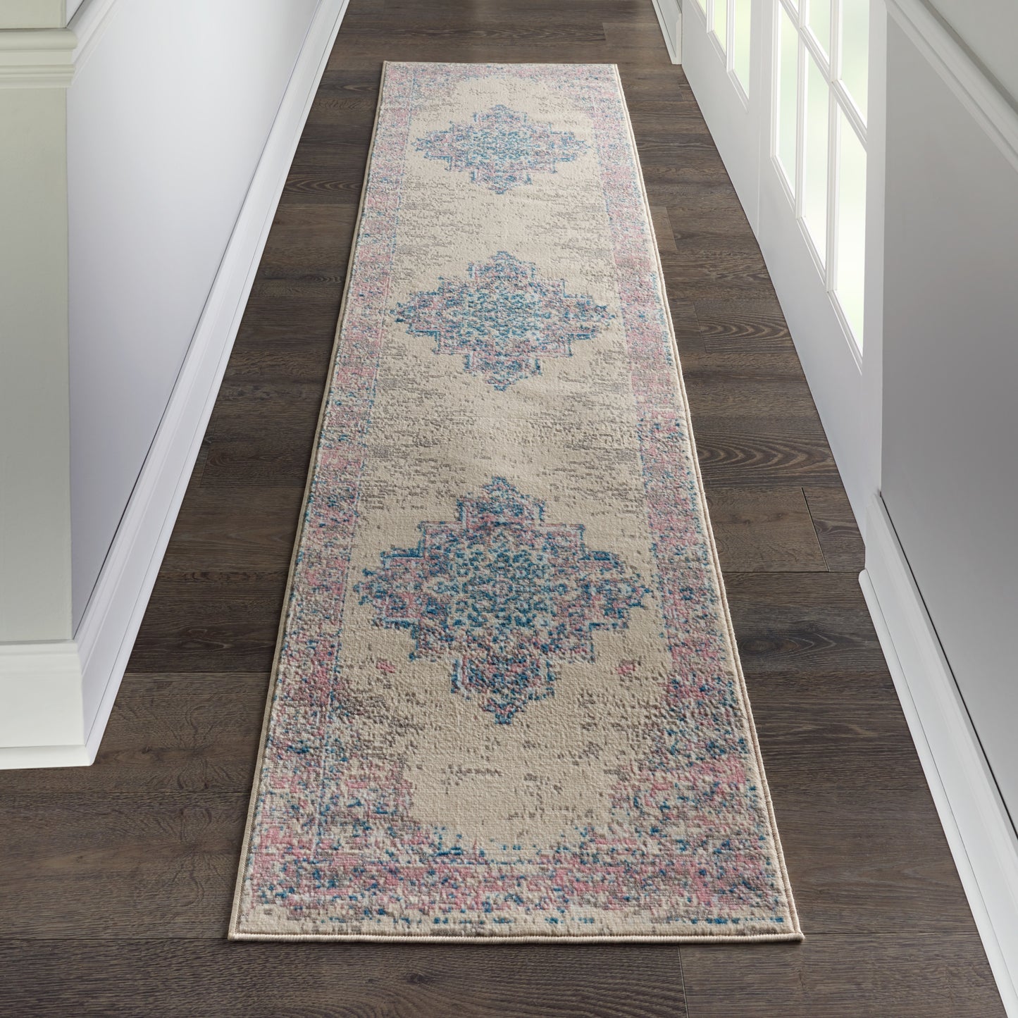 Beige distressed hallway runner rug with blue diamond medallions & pink border on dark wood floor.