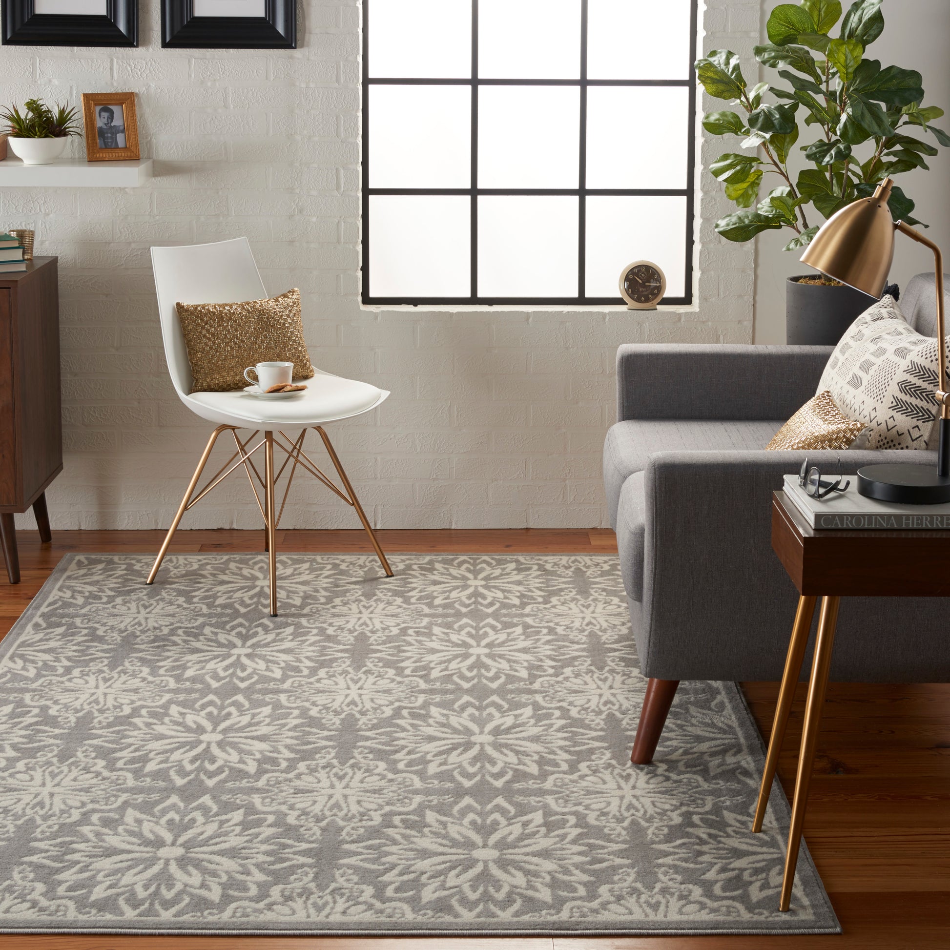 Bright living room with white mid-century chair, gray sofa, brass lamp, patterned gray rug, potted plant and grid window.