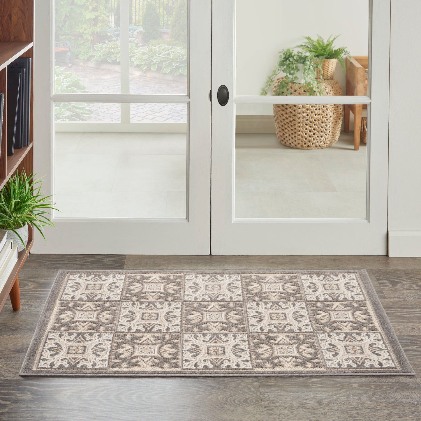 Rectangular entry rug with beige and grey tile-pattern squares, placed on wood floor by glass French doors.