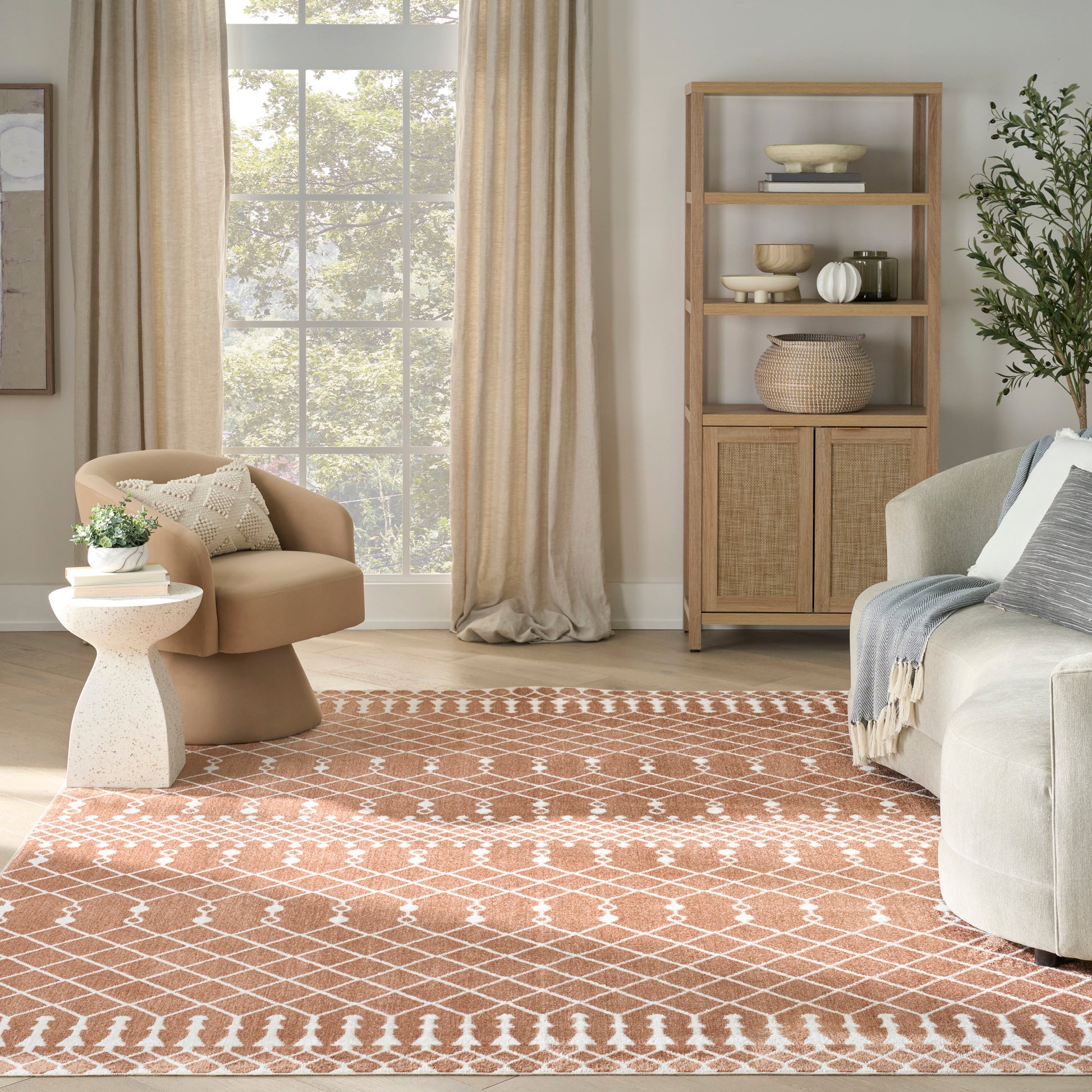 Cozy living room with tan curved armchair, orange lattice rug, light wood cabinet with woven baskets, gray sofa and plant.