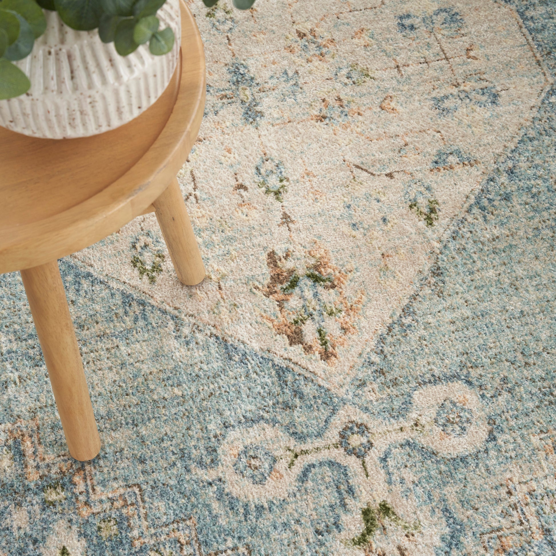 Round wooden side table with a white ribbed ceramic pot of a green plant atop a blue-beige floral oriental rug.